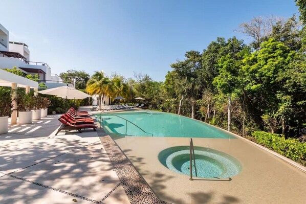 Un área de piscina con sillones de descanso, un jacuzzi y abundante vegetación.
