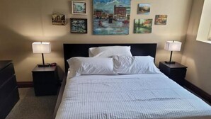 Una habitación de hotel con una cama grande, dos mesitas de noche con lámparas y cuatro cuadros en la pared.
