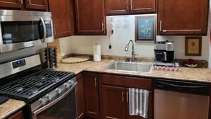 Una cocina con armarios de madera, un microondas de acero inoxidable, una estufa a gas, un fregadero y una cafetera.