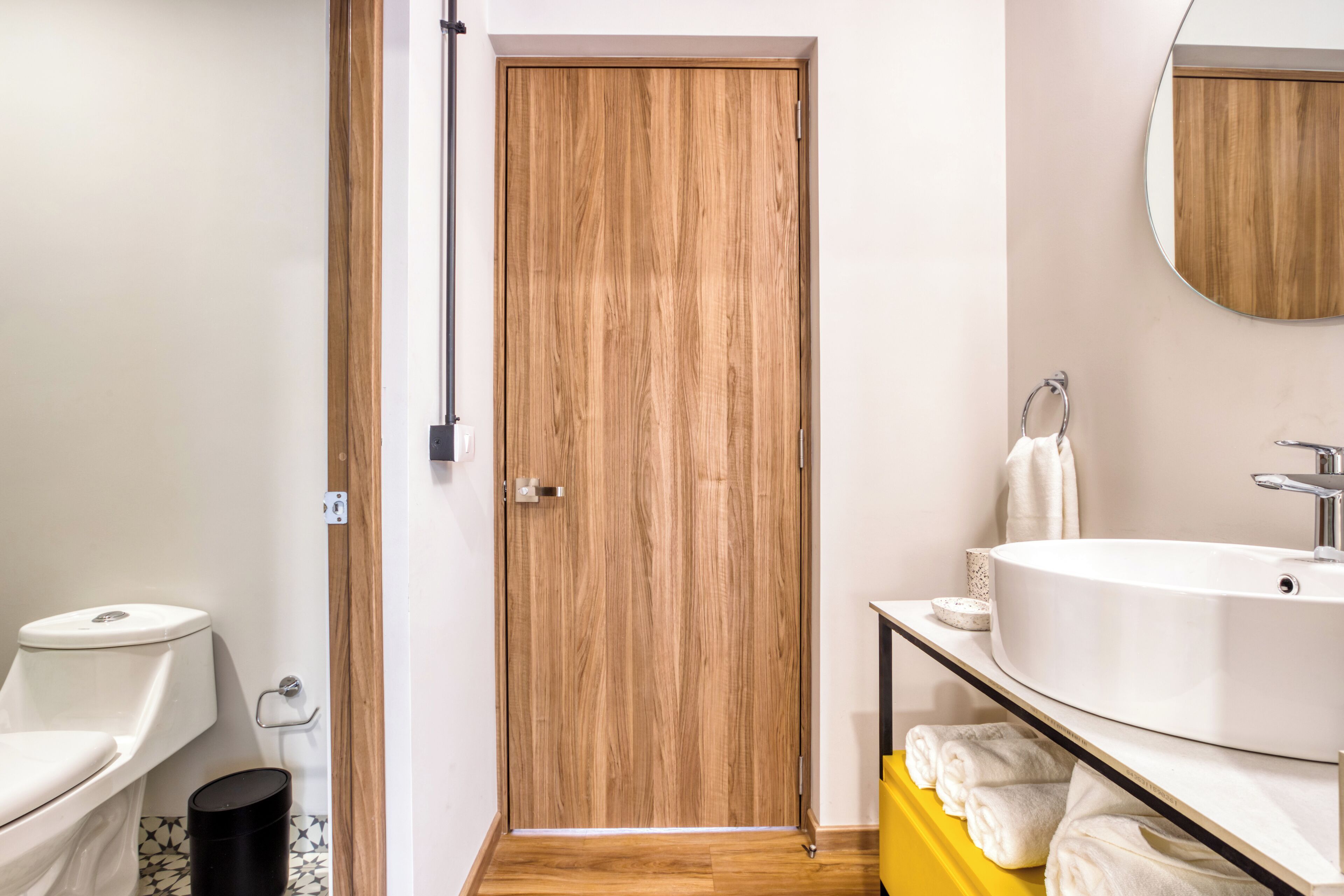 Un baño con puerta de madera, lavamanos blanco y tocador amarillo.