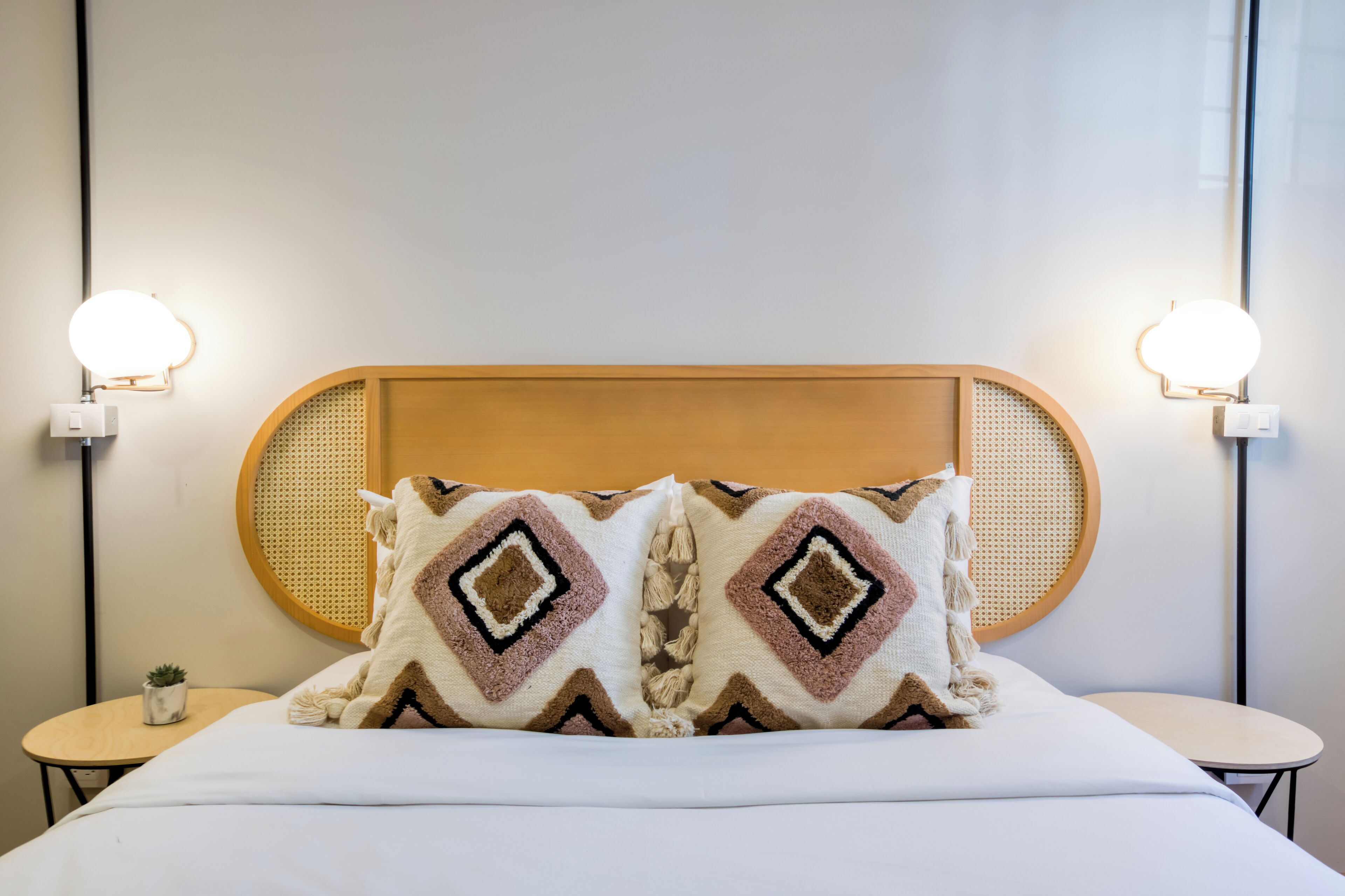 A neatly made bed with a wooden headboard, two decorative pillows, and bedside tables with wall-mounted lamps.