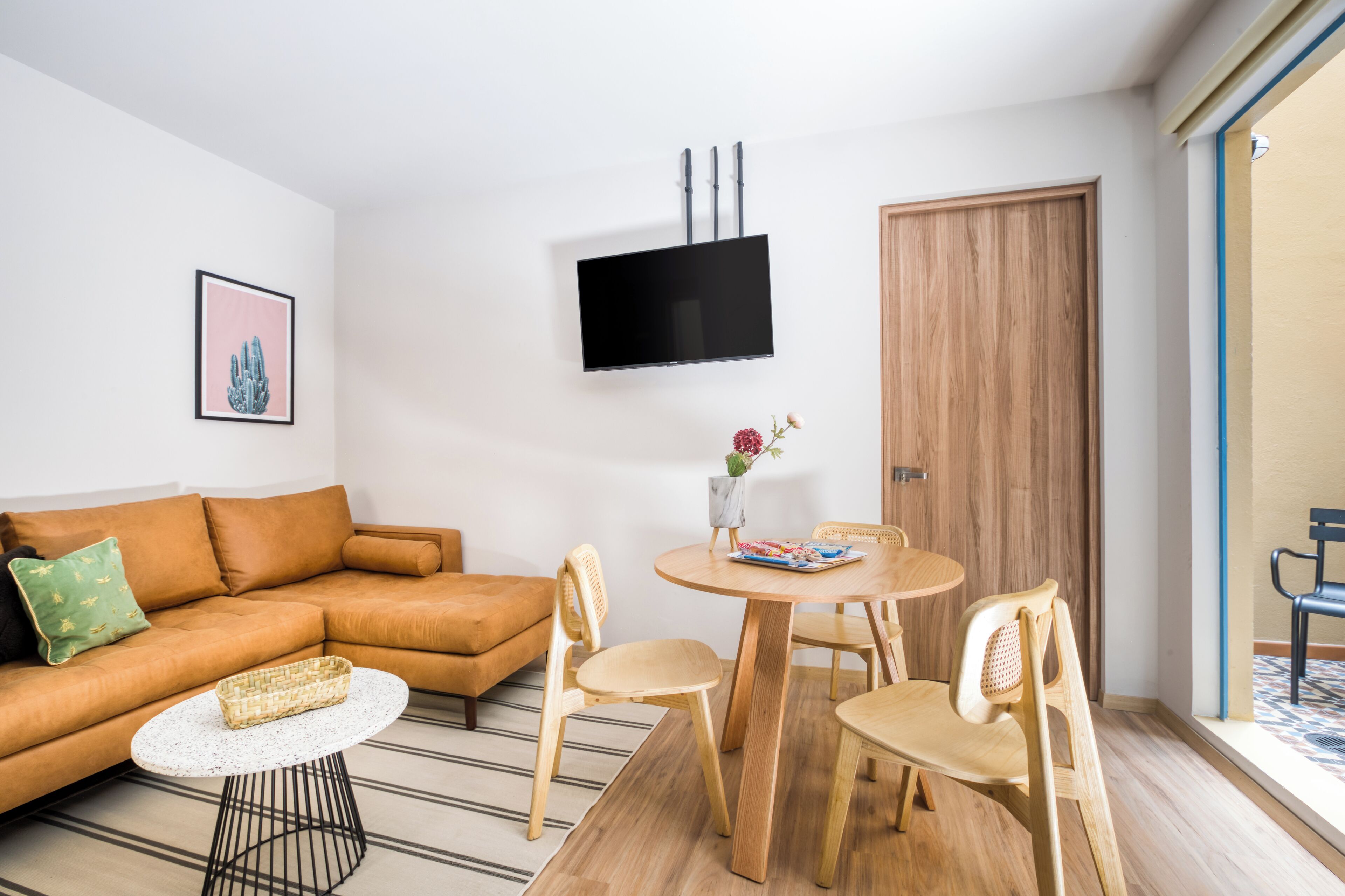 Una sala de estar moderna con un sofá, una mesa de centro, un televisor montado en la pared y una mesa de comedor con sillas.