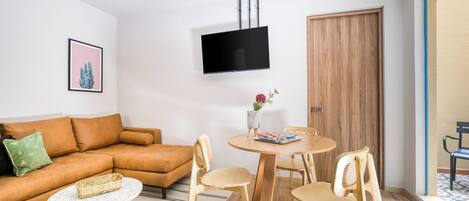 Una sala de estar moderna con un sofá, una mesa de centro, un televisor montado en la pared y una mesa de comedor con sillas.