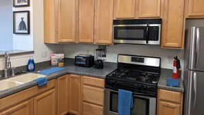 Una cocina con armarios de madera, un microondas de acero inoxidable, una estufa a gas y un refrigerador.