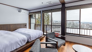 Habitación de hotel con dos camas, un balcón que ofrece vistas a árboles nevados y una zona de estar con una mesa.