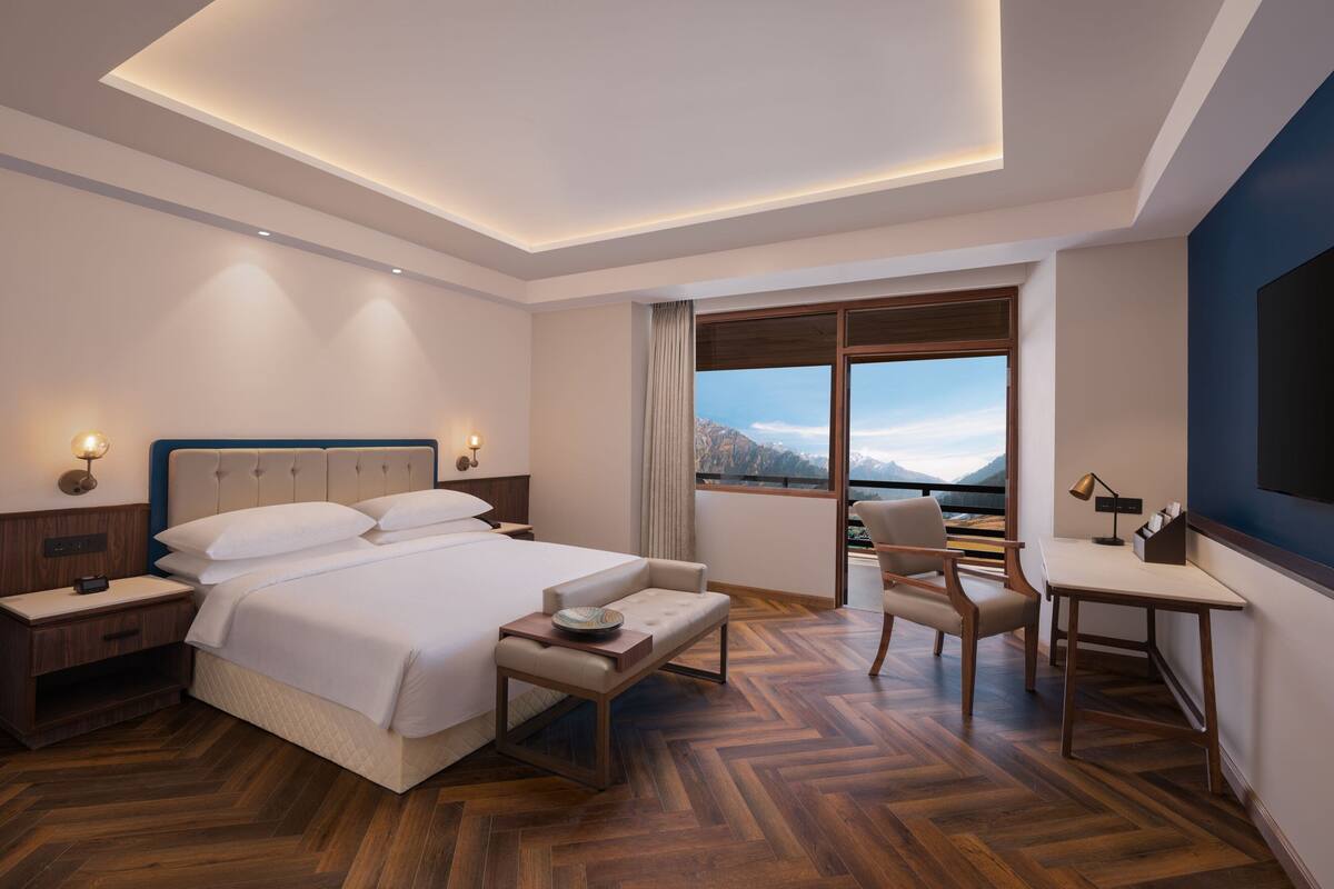 Quarto de hotel moderno com uma cama grande, uma escrivaninha e vista para montanhas.