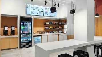 A modern cafe interior with a white counter, black stools, a beverage refrigerator, and a menu display.