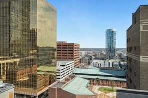 A high-rise building with a glass facade, a parking garage, and a green-roofed building in the foreground. - Aloft by Marriott Indianapolis Downtown (Indianapolis)