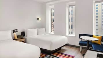 Ein modernes Hotelzimmer mit zwei Betten, einem kleinen Tisch und Blick auf die Stadt.