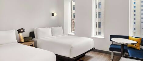 Ein modernes Hotelzimmer mit zwei Betten, einem kleinen Tisch und Blick auf die Stadt.
