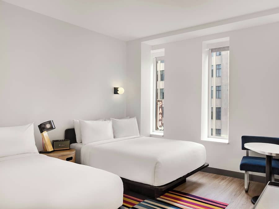 Ein modernes Hotelzimmer mit zwei Betten, einem kleinen Tisch und Blick auf die Stadt.