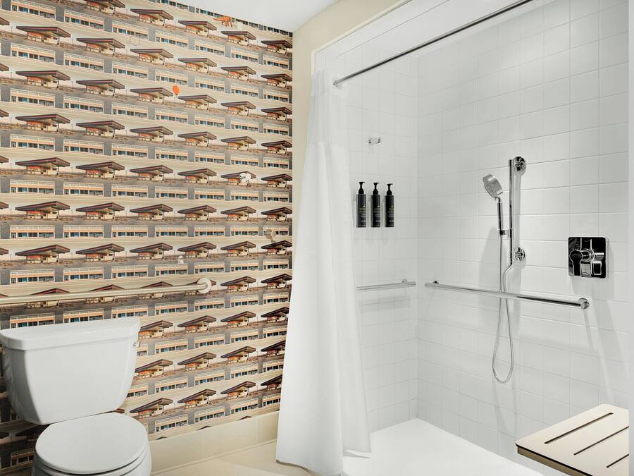 Un baño con papel tapiz estampado, un inodoro blanco, ducha con cerramiento de vidrio y un perchero para toallas.