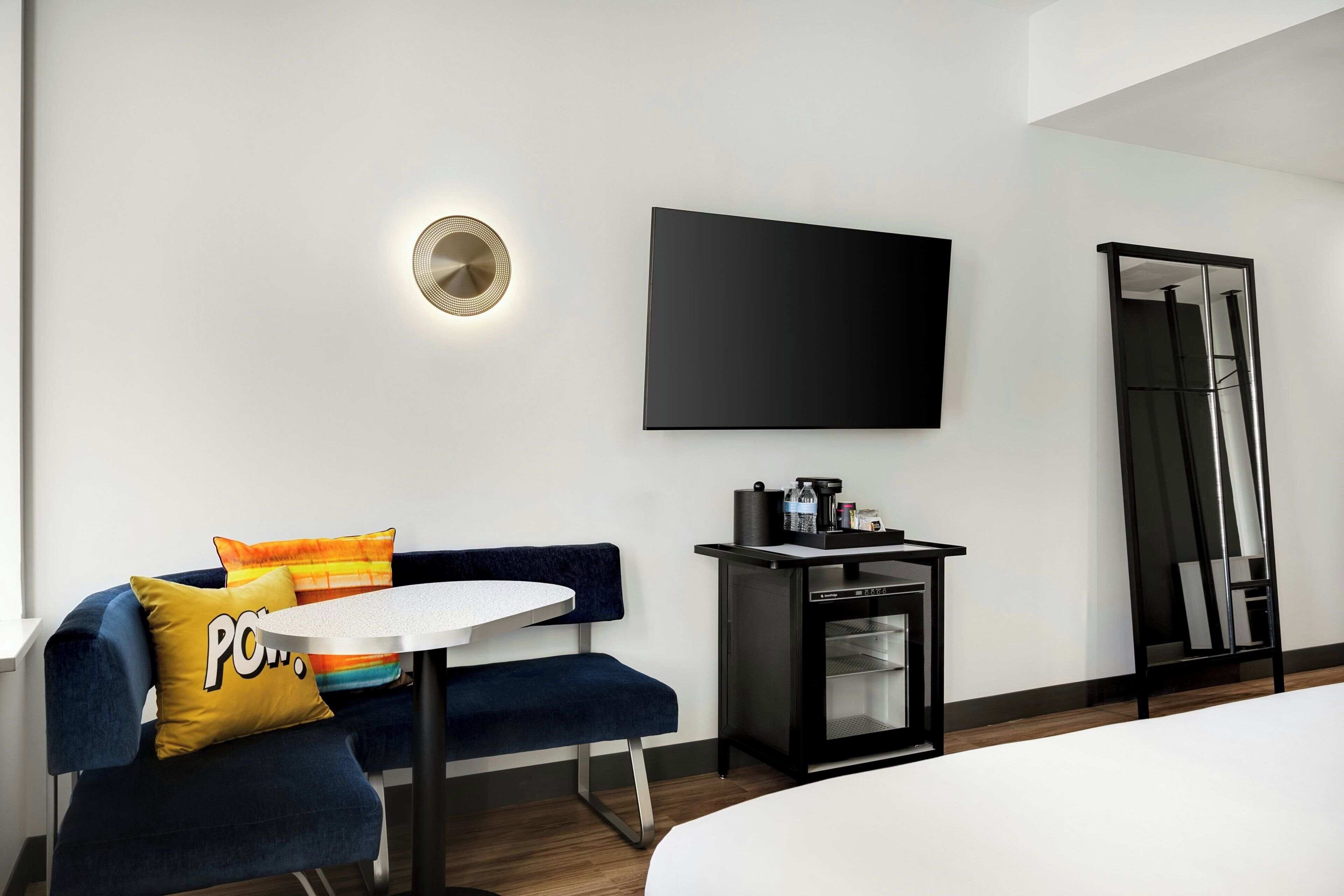 Een moderne hotelkamer met een bank, een tafeltje, een flatscreen televisie aan de muur, een koffieapparaat en een spiegel.