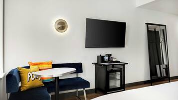 Een moderne hotelkamer met een bank, een tafeltje, een flatscreen televisie aan de muur, een koffieapparaat en een spiegel.