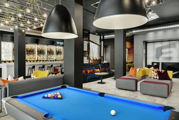 A modern lounge area with a pool table, comfortable seating, and a bar with a neon sign. - Aloft by Marriott Indianapolis Downtown (Indianapolis)