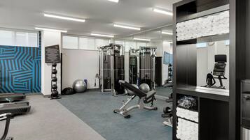Un gimnasio moderno con equipo cardiovascular, máquinas de pesas y un espejo grande.