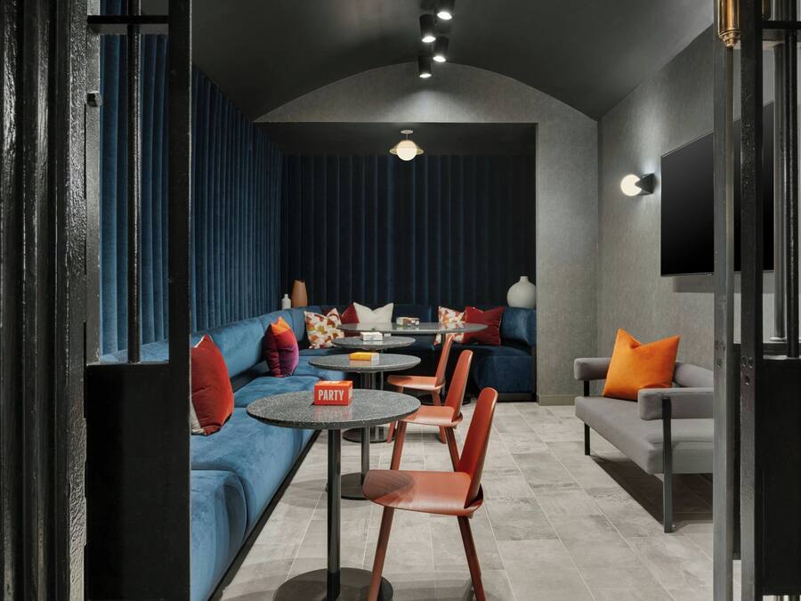 A modern lounge area with a blue sofa, orange chairs, and a small table with a 'PARTY' sign.