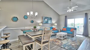 Ein modernes Wohnzimmer mit Essbereich, Deckenventilator und großem Fenster mit Vorhängen.