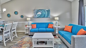 Ein Wohnzimmer mit einem blauen Sofa, orangefarbenen Kissen, einem weißen Couchtisch und einem farbenfrohen Teppich.