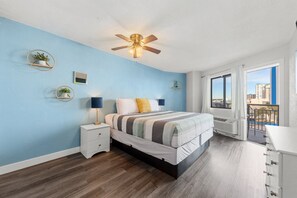Ein Schlafzimmer mit Bett, Nachttischen, Deckenventilator, Fenster mit Blick und einem Balkon.