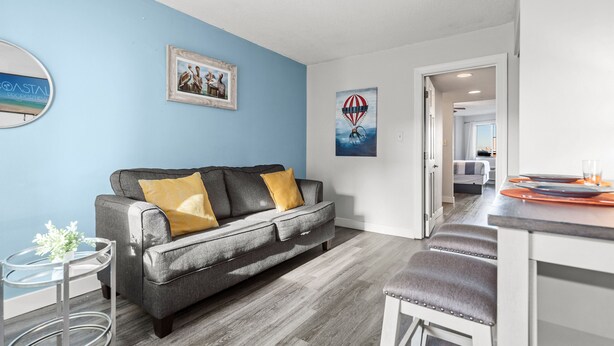 A modern living room with a grey sofa, a small round table, and a framed picture on the wall. - Chic and Charming 1BR Oceanview Suite (Myrtle Beach)