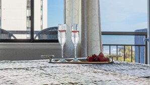 Two champagne flutes on a tray with strawberries and a small dish, set on a table with a view of the sea and buildings in the background. - Chic and Charming 1BR Oceanview Suite (Myrtle Beach)