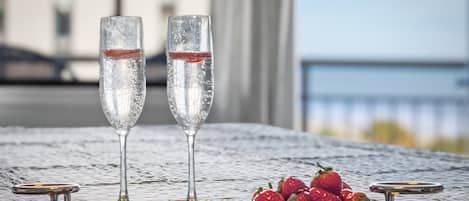 Two champagne flutes on a tray with strawberries on a textured tablecloth, overlooking a body of water.
