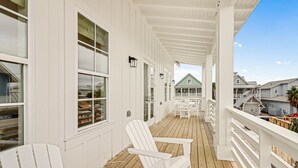 En vit träveranda med vita Adirondack-stolar, ett trädäck och utsikt över de omkringliggande husen.