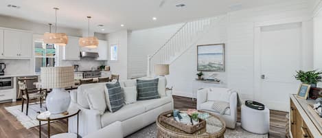 A spacious living room with a large sofa, a coffee table, and a dining area with a kitchen in the background.