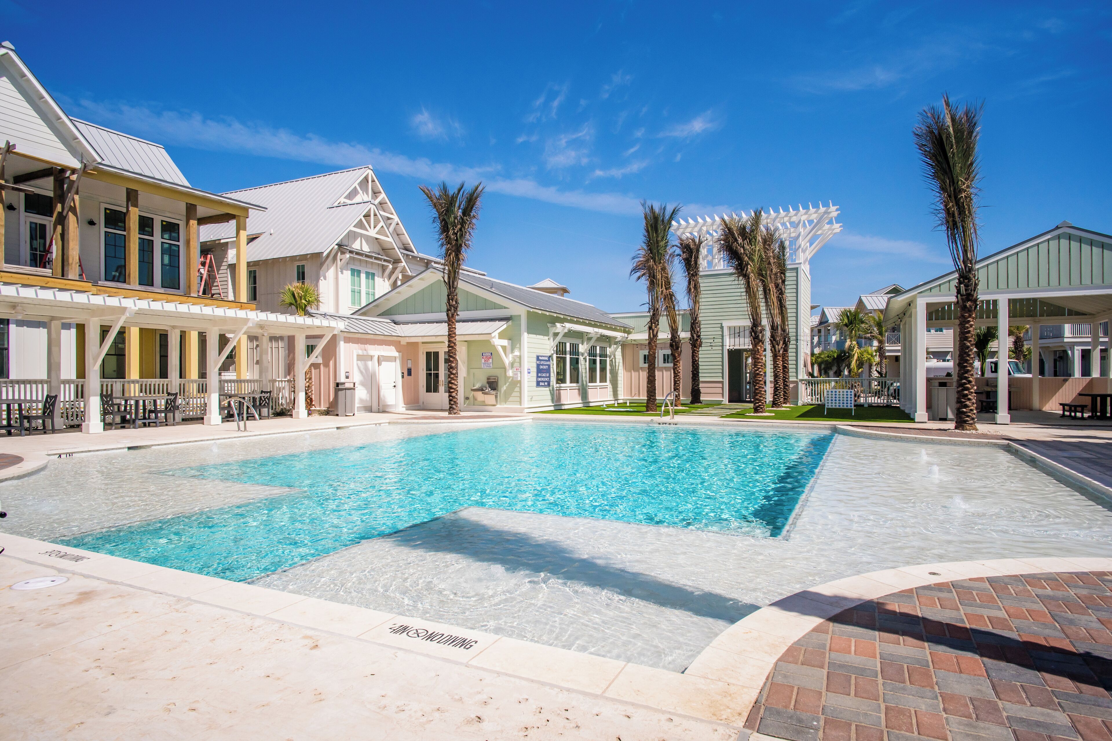 A swimming pool area with a clear blue pool, surrounded by buildings with balconies and palm trees.