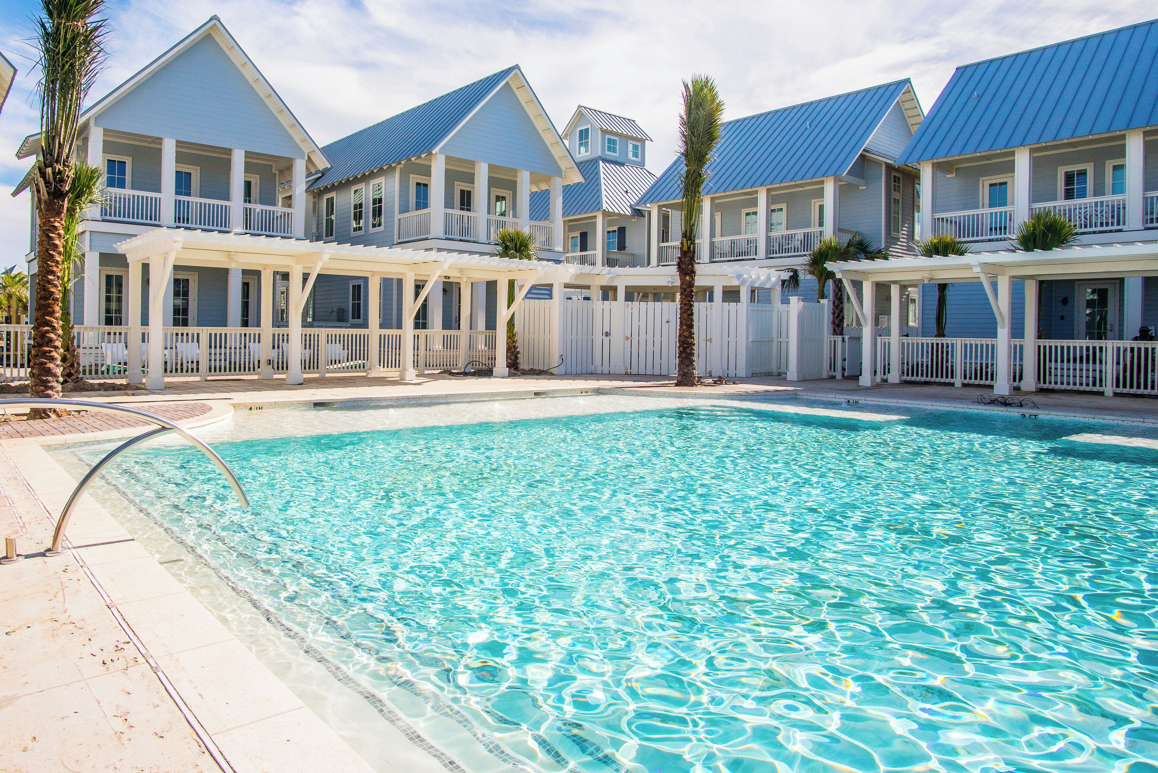 A pool area with a clear blue pool, white railings, and a series of blue-roofed buildings with balconies.