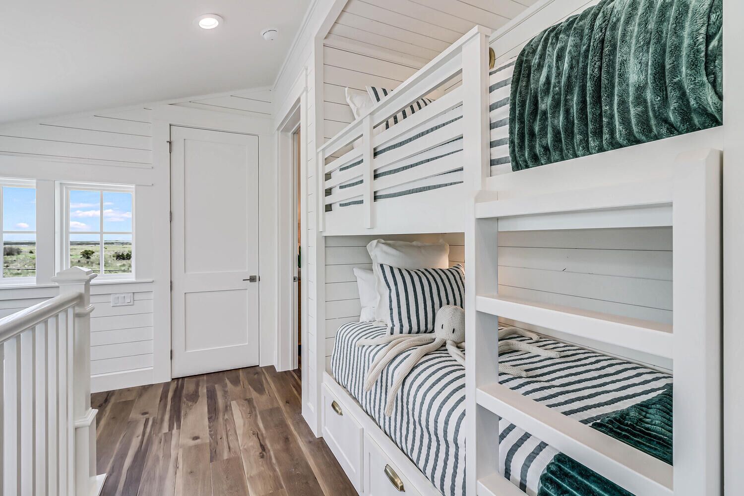 A bedroom with bunk beds, a window with a view, and a wooden floor.
