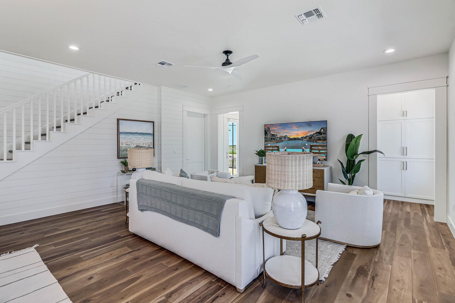 A spacious living room with a white staircase, a sofa, a round table, and a large window with a view.