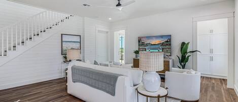 A spacious living room with a white staircase, a sofa, a round table, and a large window with a view.