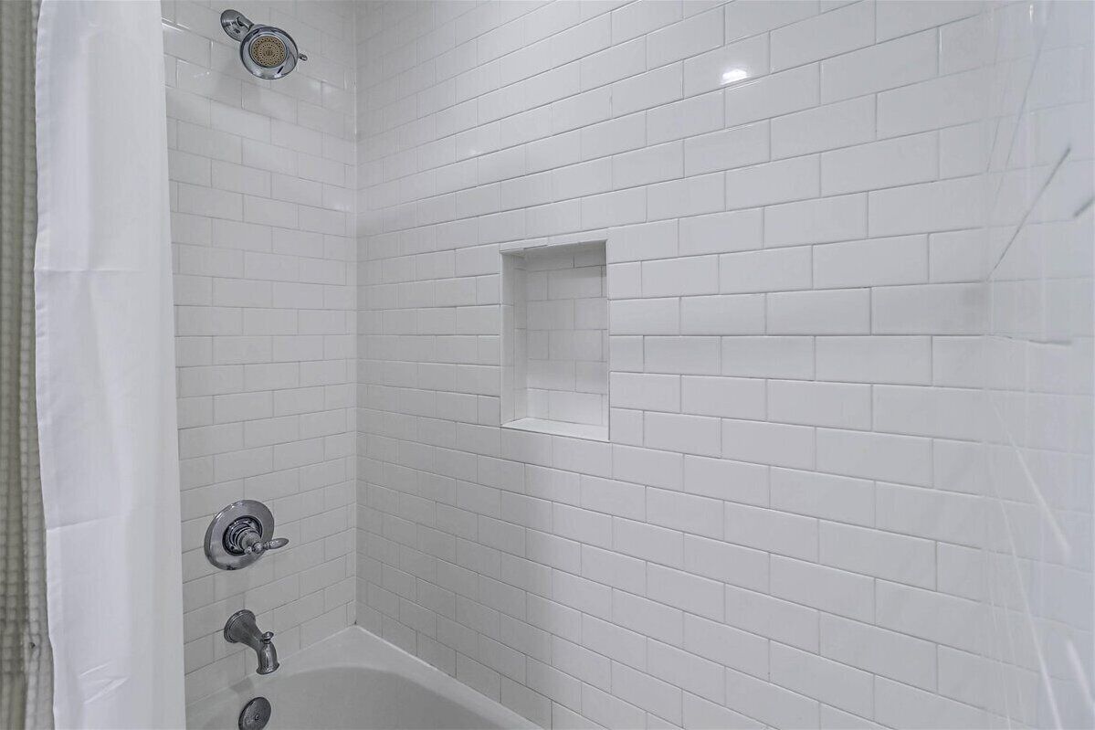 A bathroom with white subway tiles, a showerhead, a bathtub, and a small square tile accent.