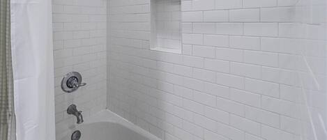 A bathroom with white subway tiles, a showerhead, a bathtub, and a small square tile accent.