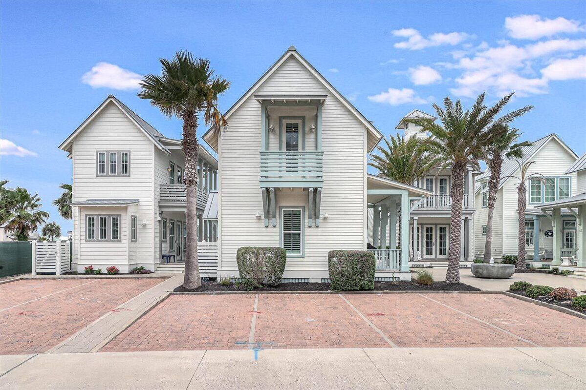 A two-story house with a central balcony, a front porch, and a driveway with a brick pattern.