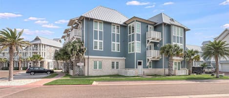 Un edificio residencial de varios pisos con fachada azul, detalles blancos y techo inclinado.