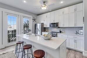 A modern kitchen with white cabinetry, a large island with stools, stainless steel appliances, and a ceiling fan.