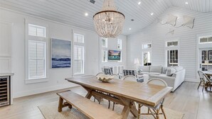 A spacious room with a large wooden dining table, a bench, and a chandelier. There are two sofas and a television mounted on the wall. - Sunnyside Up 209 LAK (Port Aransas)