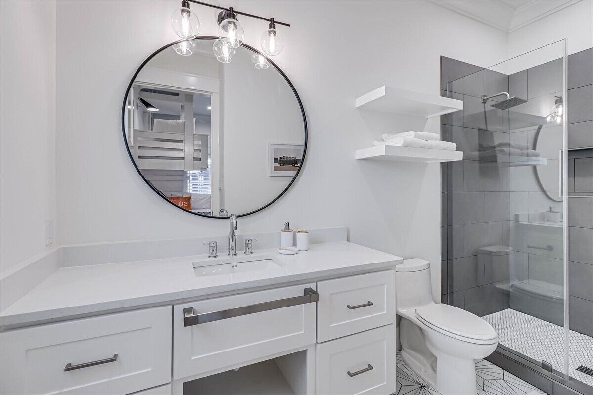 Une salle de bain moderne avec un grand miroir rond, un meuble-lavabo blanc et une douche à parois de verre.