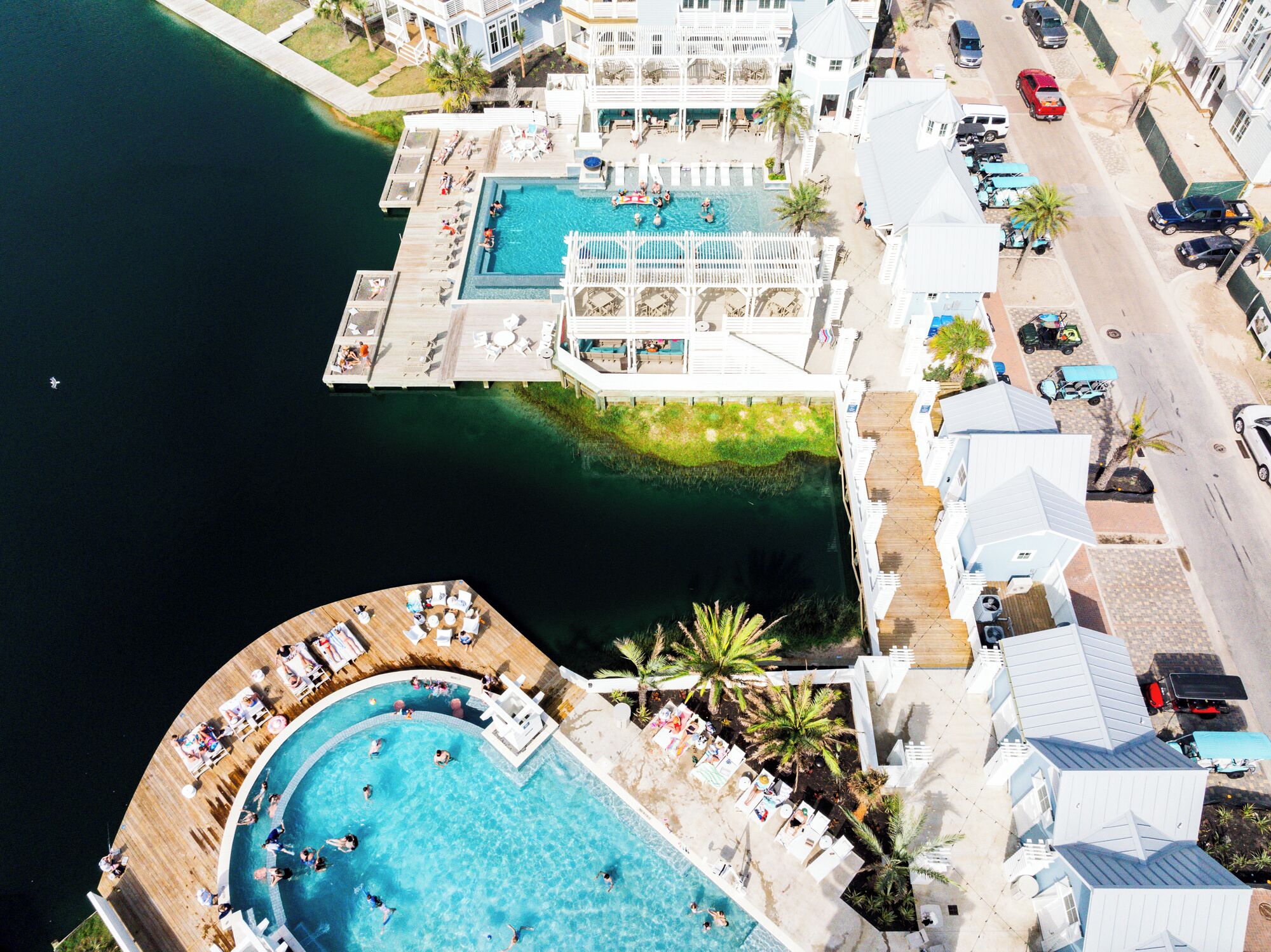 Vista aérea de un complejo turístico con una gran piscina central, una piscina más pequeña y una zona de embarcadero.