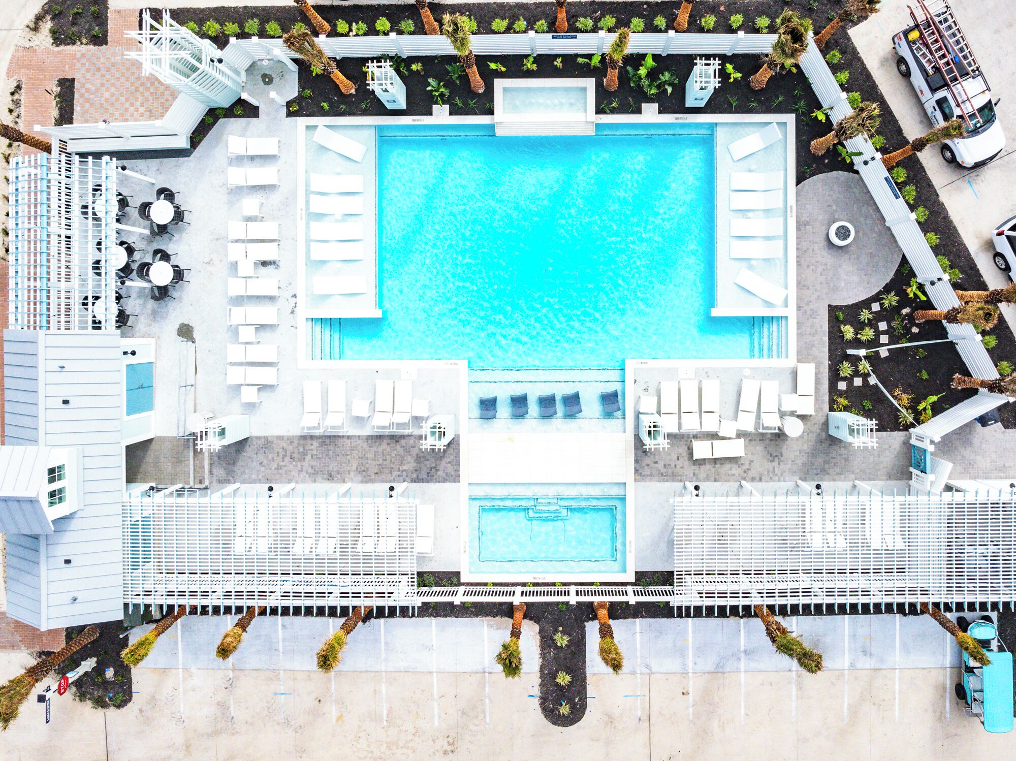 An aerial view of a hotel with a central swimming pool, multiple lounge areas, and a parking lot.