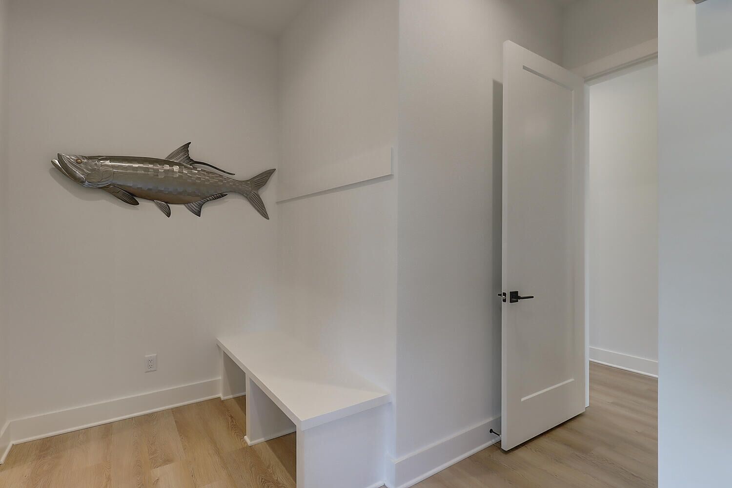 A hallway with a white door, a white bench, and a fish decoration on the wall.
