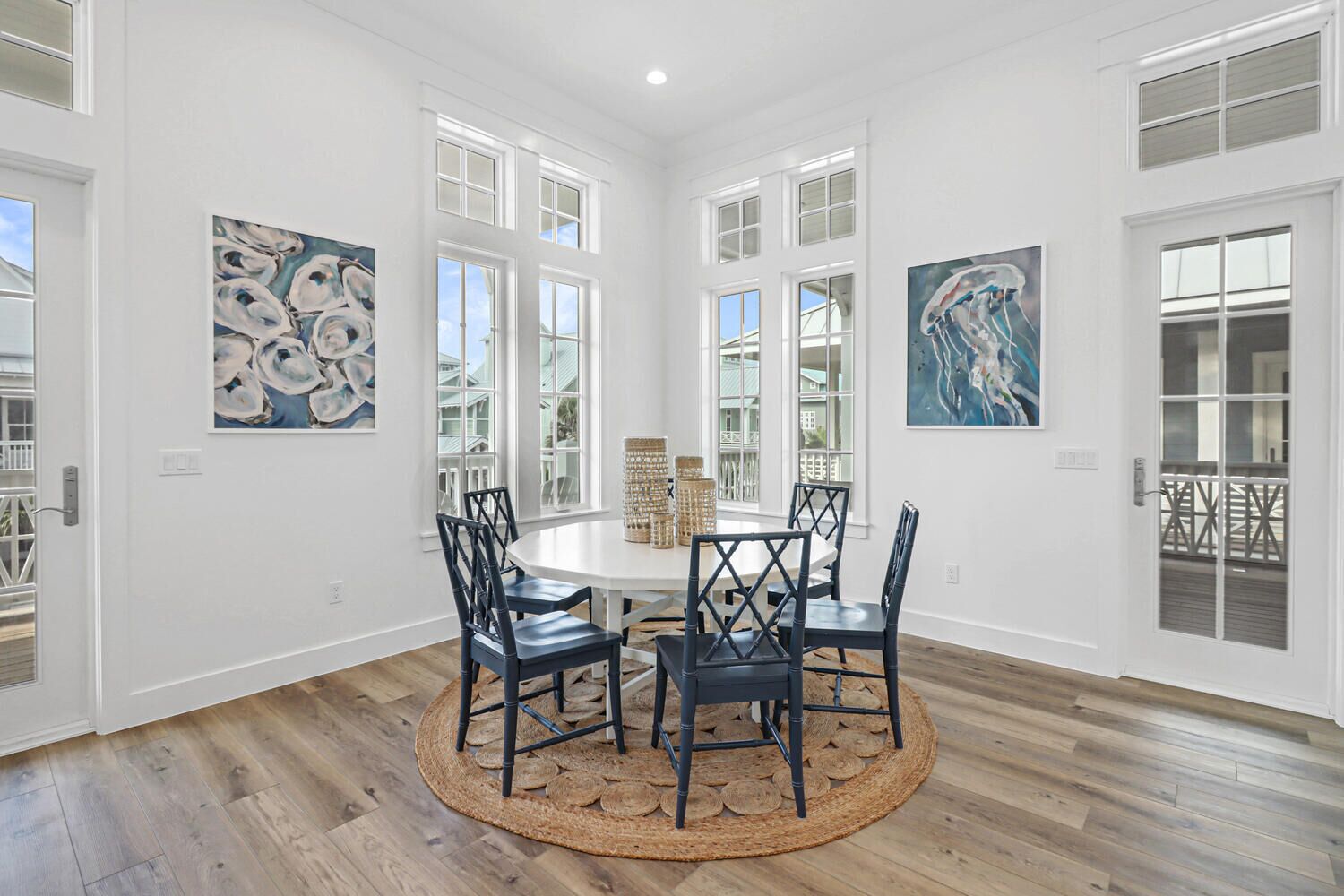 A dining room with a round table, four chairs, and two paintings on the walls.