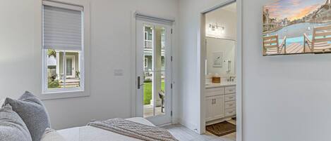 A bedroom with a bed, a window, a door leading to a bathroom, and a painting on the wall.