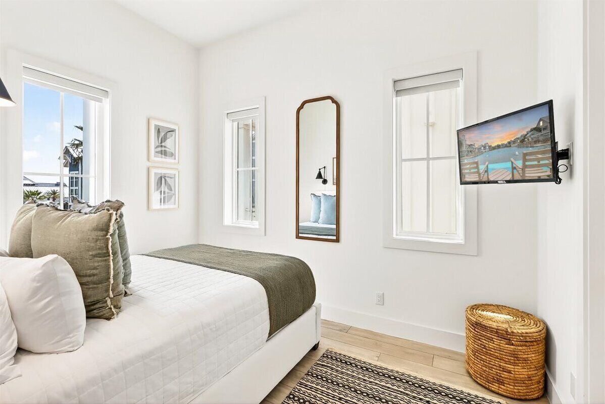 A bedroom with a bed, a mirror, a television, and a window with a view of a dock and water.