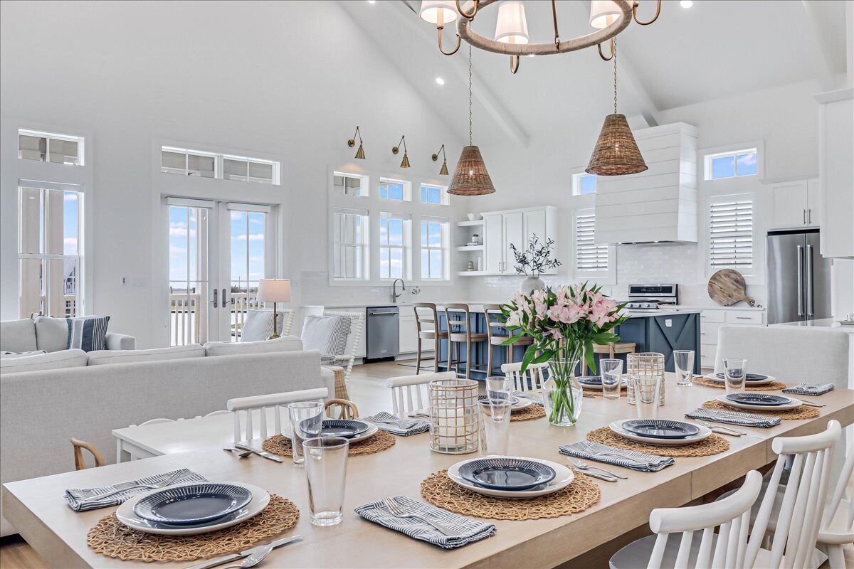 Una cocina amplia con armarios blancos, un comedor con una mesa grande dispuesta para seis personas, y una zona de estar acogedora con un sofá y sillones.