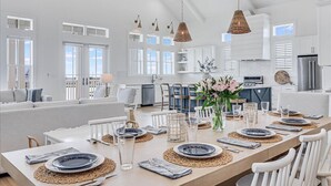 Een ruime keuken met witte kasten, een eethoek met een lange tafel voor zes personen, en een gezellig zithoek met een bank en stoelen.