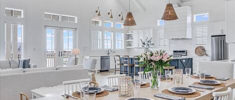 Una cocina amplia con armarios blancos, un comedor con una mesa grande dispuesta para seis personas, y una zona de estar acogedora con un sofá y sillones.